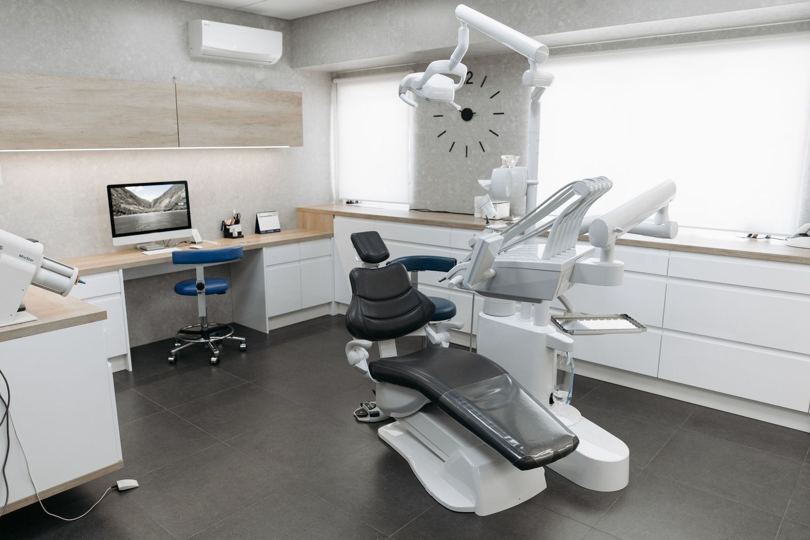 A bright, uncluttered dental treatment room with a chair, screen, and pale wood cabinetry.